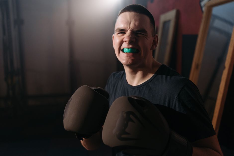 A determined boxer with gloves and mouthguard in an indoor setting, ready for action.