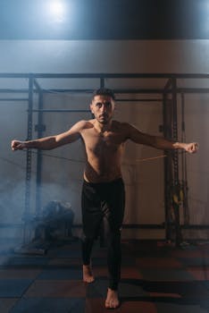 Shirtless man exercising with resistance band in gym, showcasing determination and fitness.
