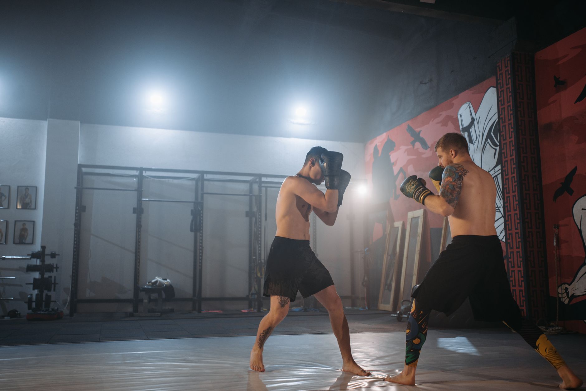 Two muscular men sparring in an MMA gym with gloves, showcasing fitness and combat skills.