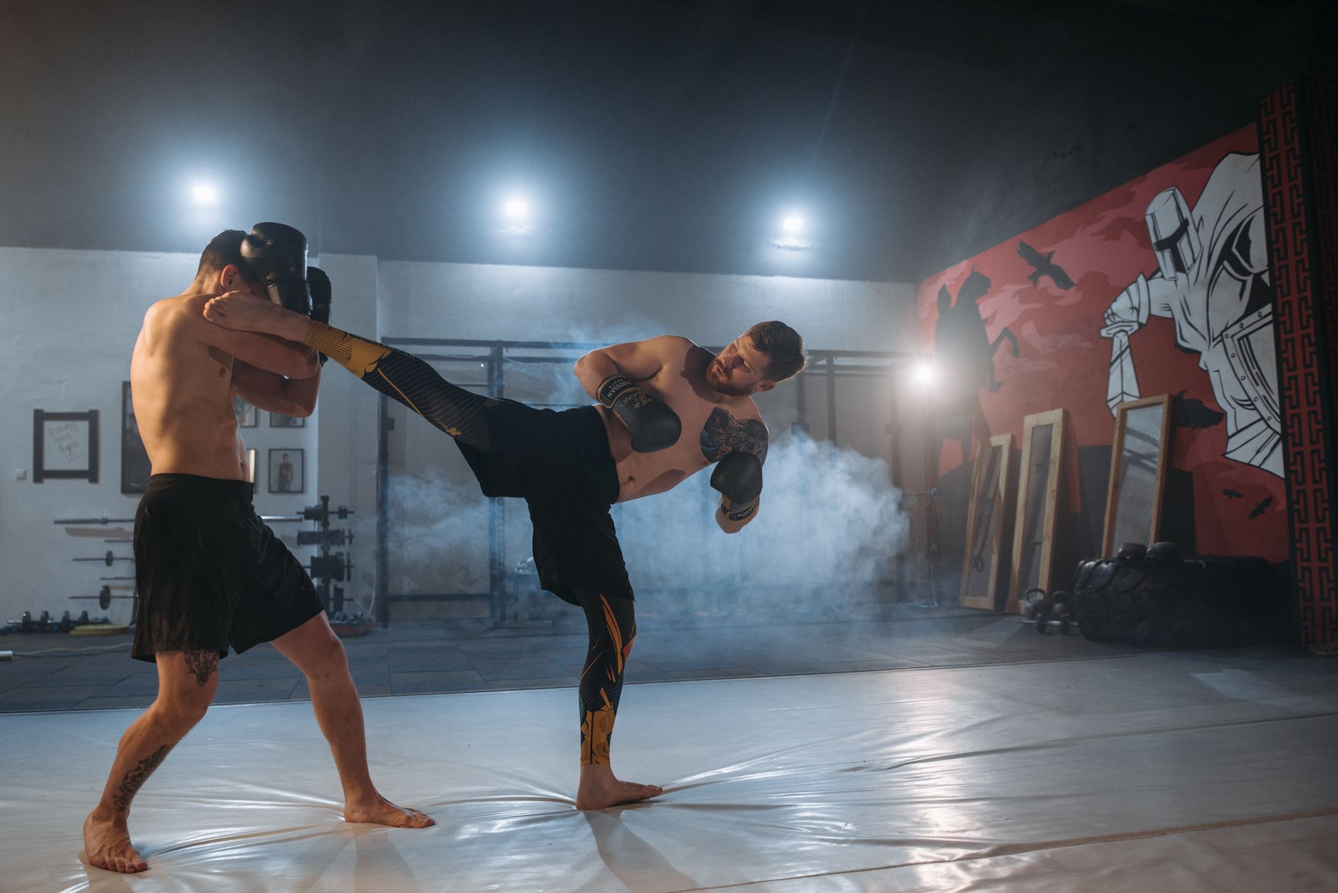 Two male fighters practice kickboxing techniques in a gym, emphasizing strength and agility.