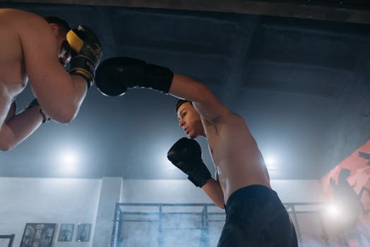 Two shirtless boxers sparring intensely in a gym, showcasing strength and agility.