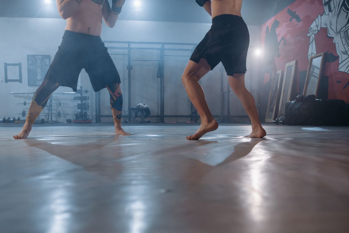 Two athletes practicing boxing footwork barefoot in a gym