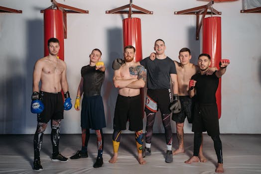 Six male boxers standing confidently in a gym with red punching bags.