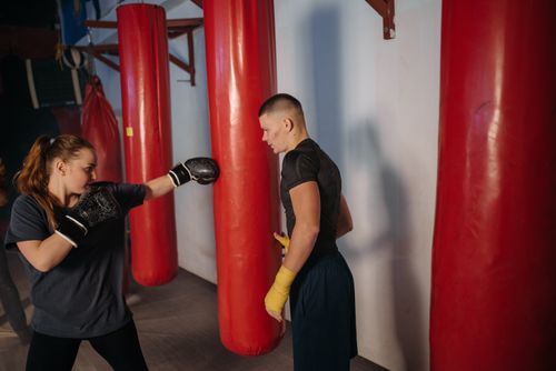 Free Woman and trainer in boxing gym, engaging in intense punch training with red bags. Stock Photo