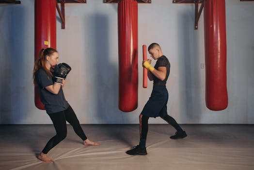 Female boxer and male trainer practicing in an indoor boxing gym with red punching bags.