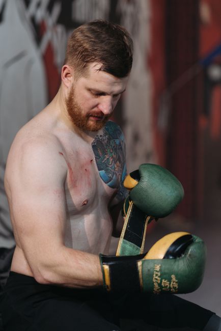 Fotomural Un fuerte boxeador tatuado con guantes sentado y preparándose para una pelea en interiores.