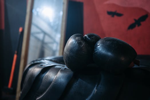 Close-up of black boxing gloves resting on a tire in a dimly lit gym setting, conveying a gritty training atmosphere.
