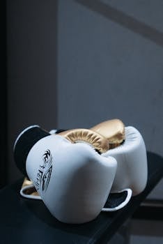 White and gold boxing gloves resting elegantly on a black surface, highlighting their premium quality.