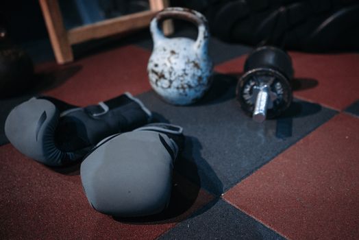 Close-up of gym equipment including a kettlebell, dumbbell, and boxing gloves on a gym floor.