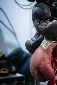 Weathered boxing gloves hanging in an indoor gym setting, with depth of field detail.