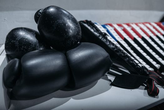 Close-up shot of black boxing gloves placed on a table with martial arts gear in a dimly lit room.