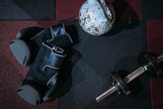 High angle view of boxing gloves, dumbbell, and kettlebell on gym floor.