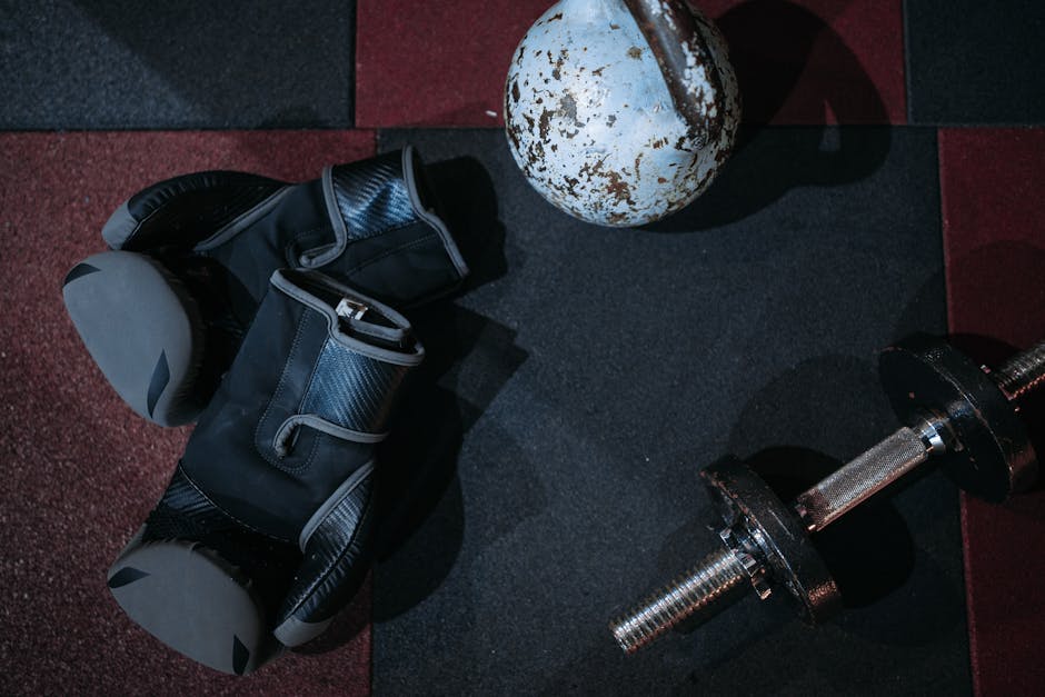 High angle view of boxing gloves, dumbbell, and kettlebell on gym floor.