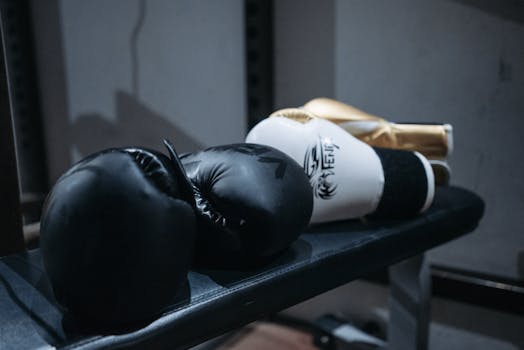 Close-up of black and white boxing gloves resting on a gym bench indoors, with a focus on sports equipment.