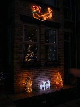 Illuminated Christmas decorations with sleigh, reindeer, and trees outside a house at night.