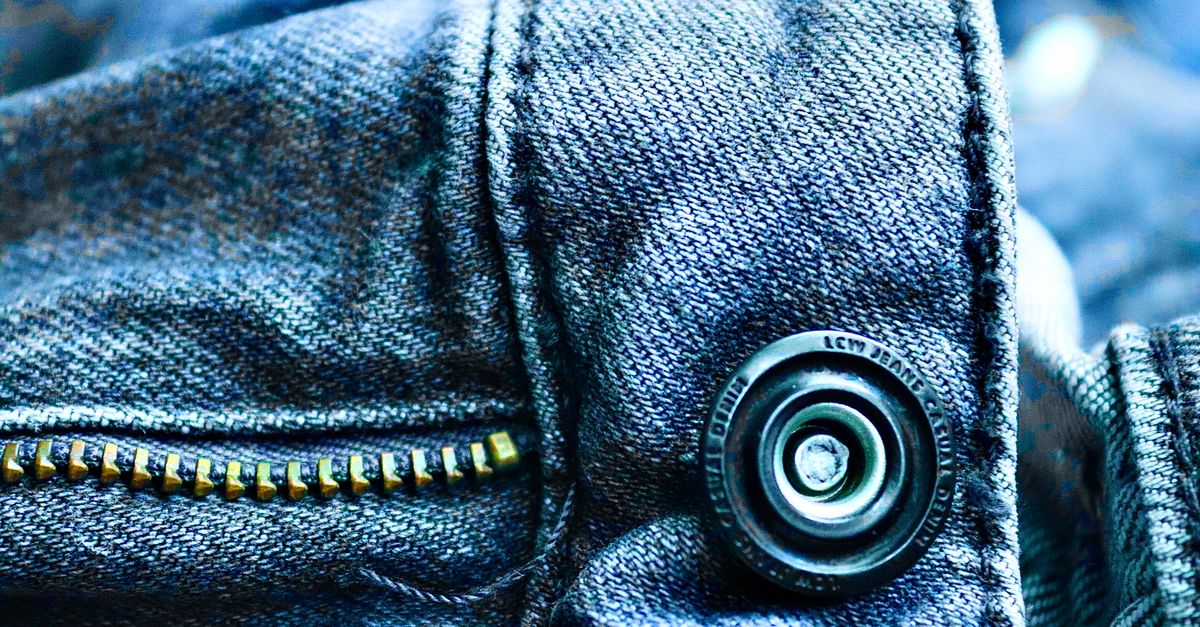 Hand die een nieuw lipje aan de schuiver van een jasrits bevestigt