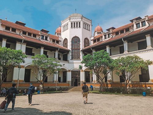 Free Lawang Sewu's courtyard with people walking under a clear blue sky, surrounded by historic architecture. Stock Photo
