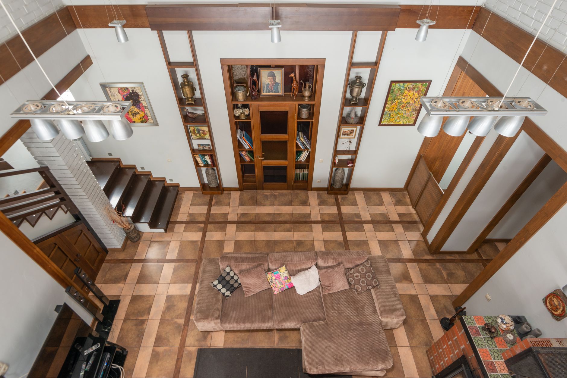 From above interior of contemporary apartment with hanging lamps over sofa in room with staircase and decorative elements on wall