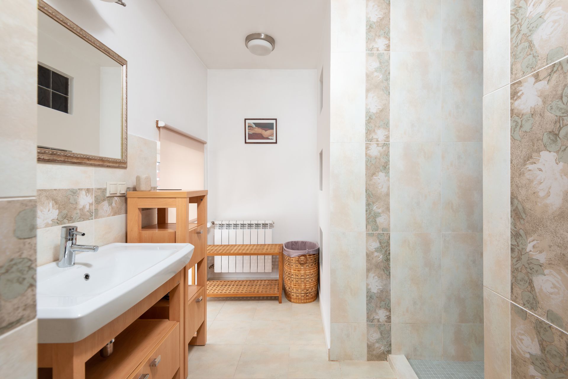 Cupboard with sink and faucet placed near wooden stand and mirror hanging on wall against wall with abstract design in bathroom