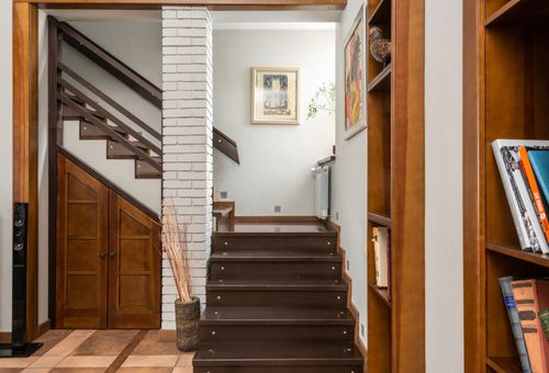 Free Wooden stairway near brick column placed at shelves with books in modern flat with pictures on wall and dry plants in vase Stock Photo