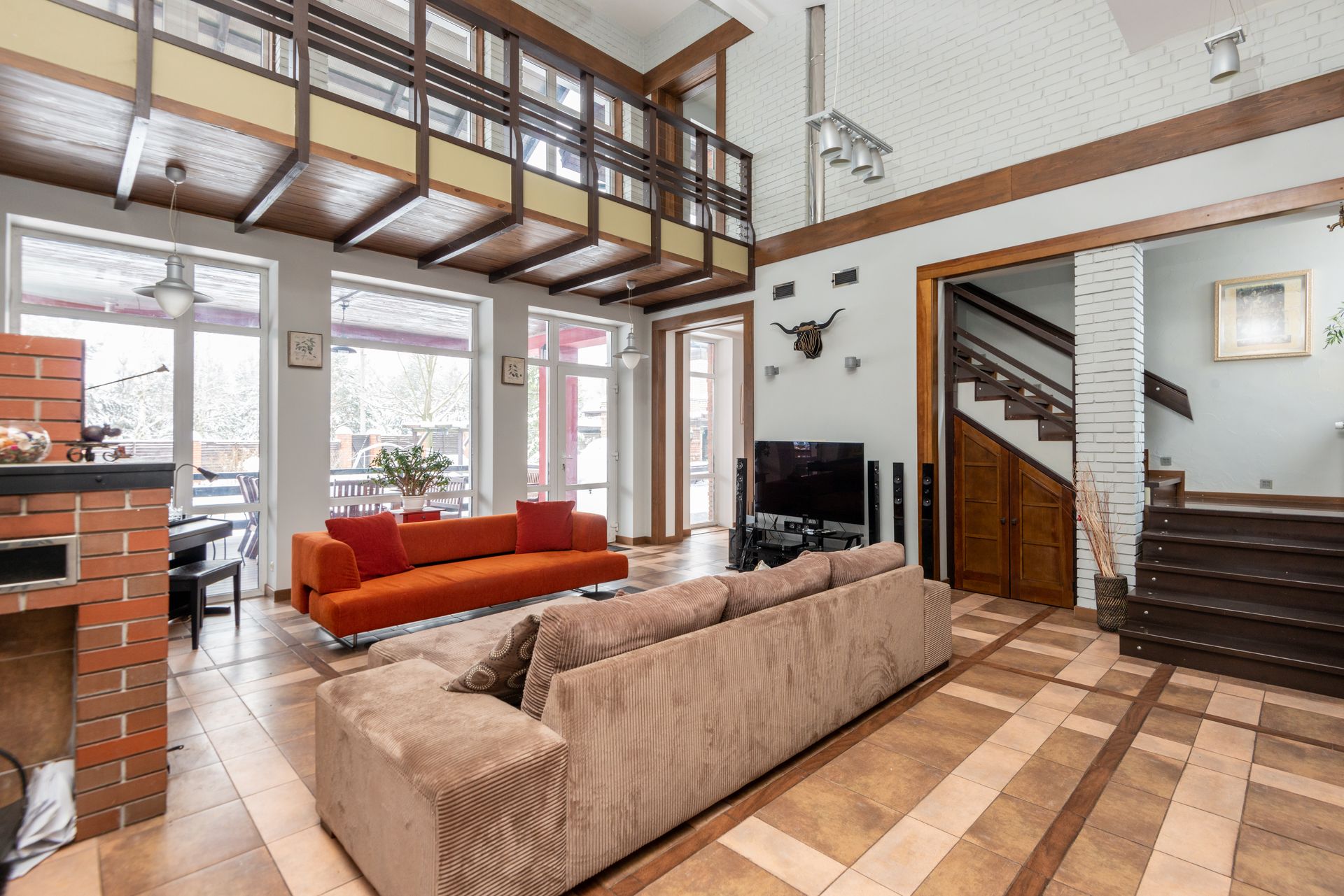 Interior of contemporary spacious apartment with comfortable sofas and big windows located in room with TV near staircase at home