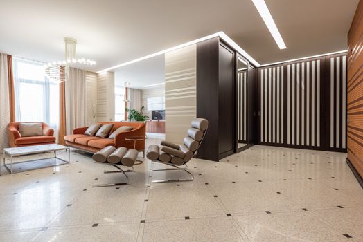 Interior of modern flat with spacious corridor and comfortable seats in living room with kitchen counter in distance at home
