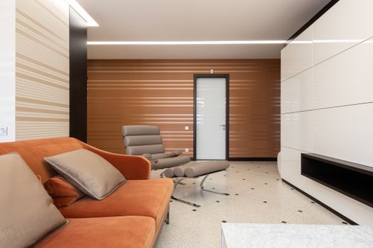Interior of modern living room with soft sofa with cushions and armchair placed against white wall and translucent door at home