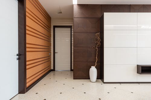 Interior of spacious hallway of modern apartment with door and white vase placed at wall on tiled floor at home