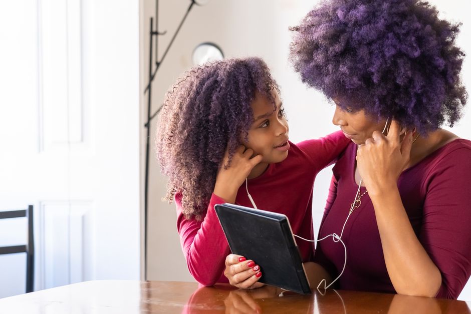 Mother and daughter with afro hair using a tablet together indoors, symbolizing love and togetherness.