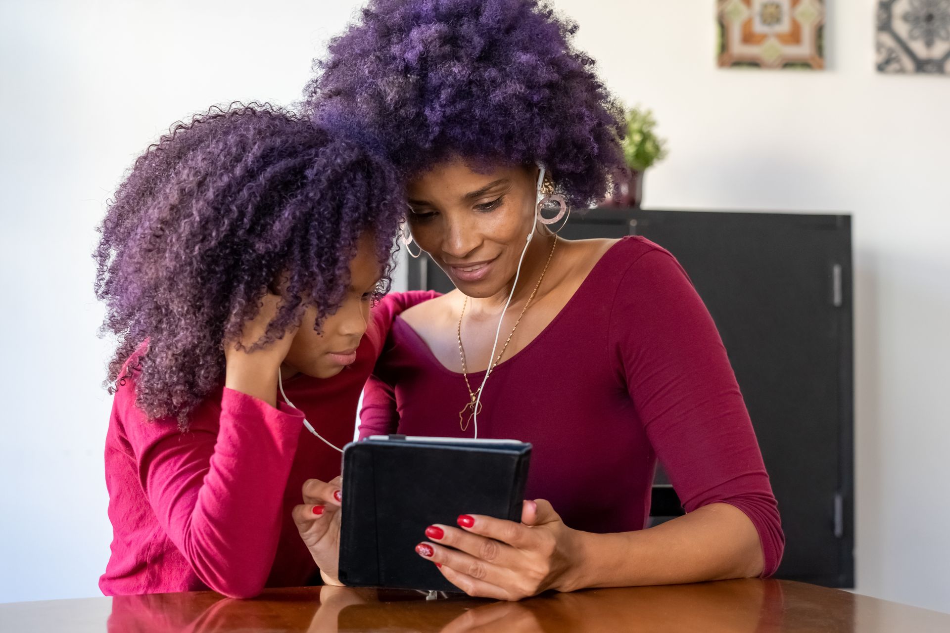 A mother and daughter sharing headphones while using a tablet, promoting family bond and technology use.