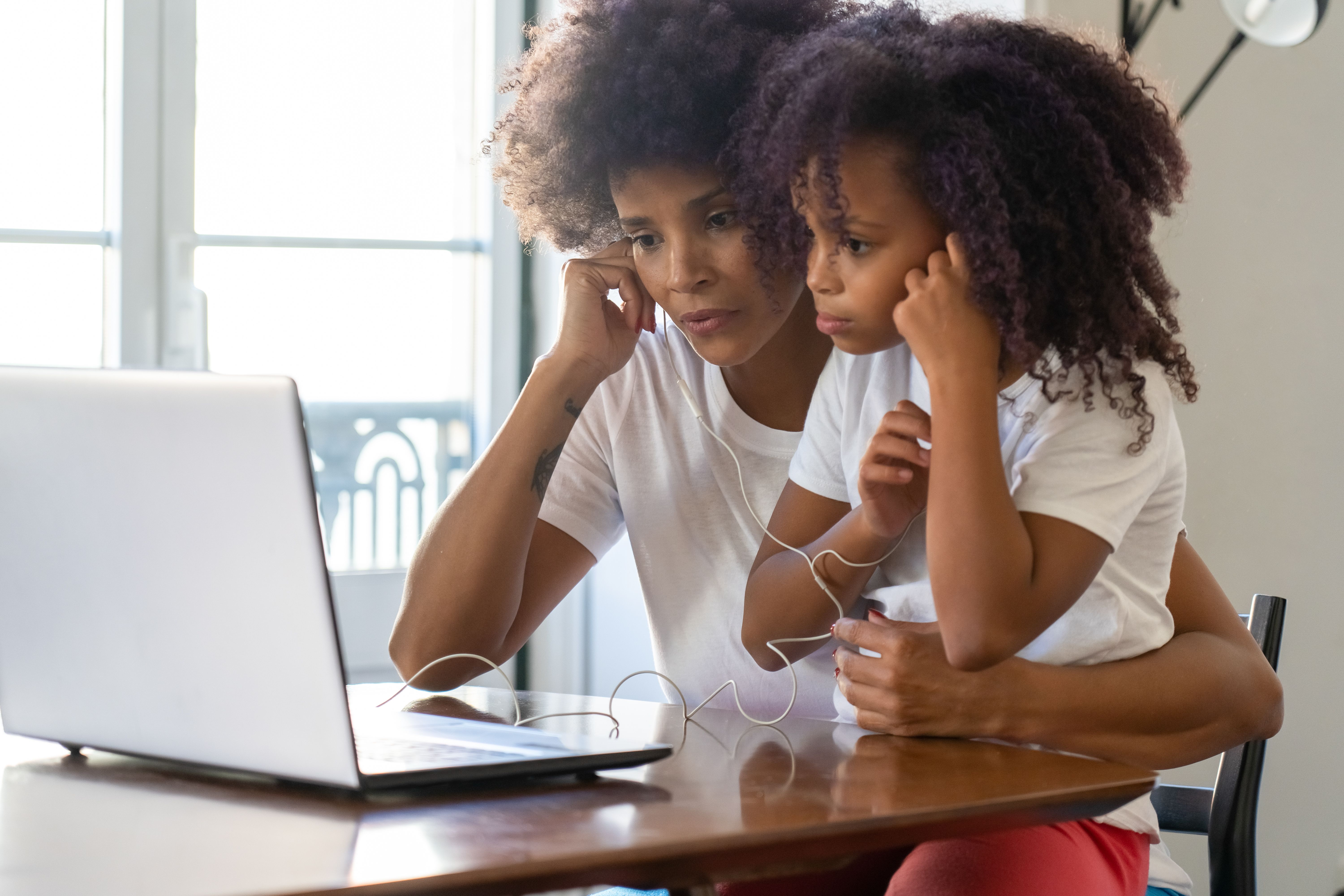 Mother and daughter sharing headphones and looking at a laptop together at home