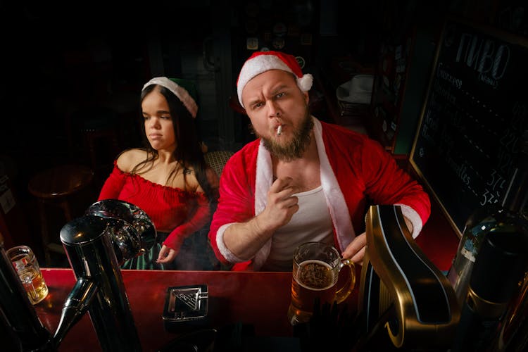 Man Dressed As Santa Claus Drinking Beer And Smoking A Cigarette With A Helper 