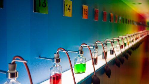 Free Row of glass bottles with colored liquids in a vibrant lab setting. Stock Photo