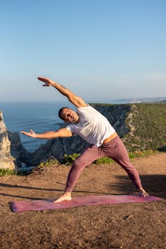 Man performing yoga stretch on cliffside overlooking the ocean in Portugal.