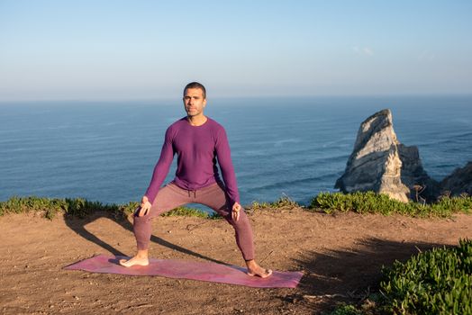 A man meditates and practices yoga on a cliffside overlooking the sea in Portugal.
