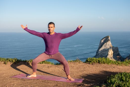 A man meditating in a yoga pose by the sea cliffs of Portugal, embracing wellness.