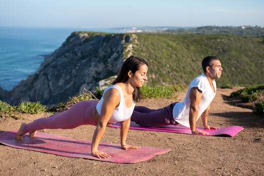 A man and woman practicing yoga on a cliffside in Portugal, enjoying outdoor exercise with a scenic view.