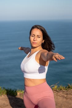 Adult woman performs yoga pose on a scenic cliffside overlooking the sea in Portugal.