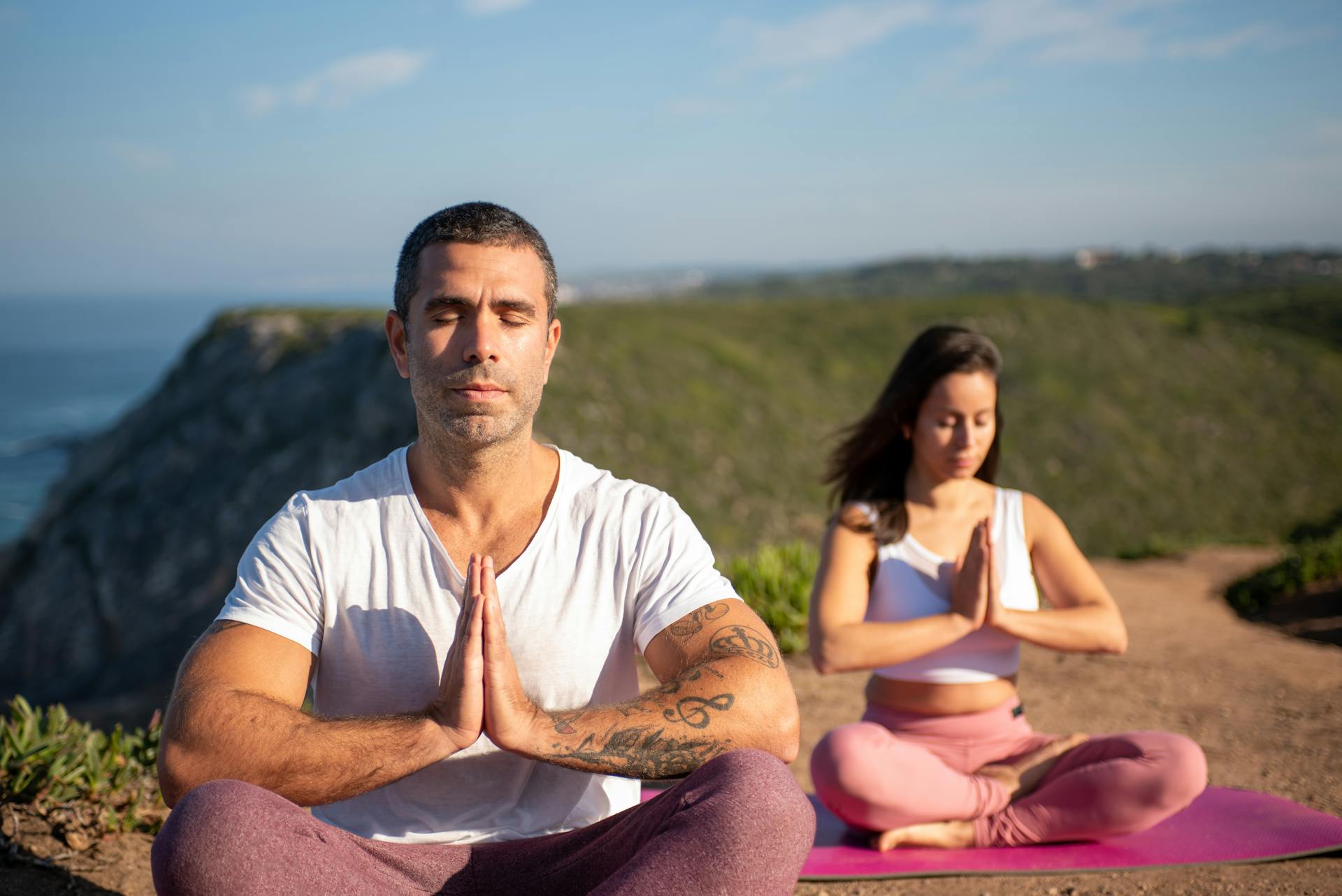 Man and woman meditating outdoors on yoga mats by the coast in Portugal.