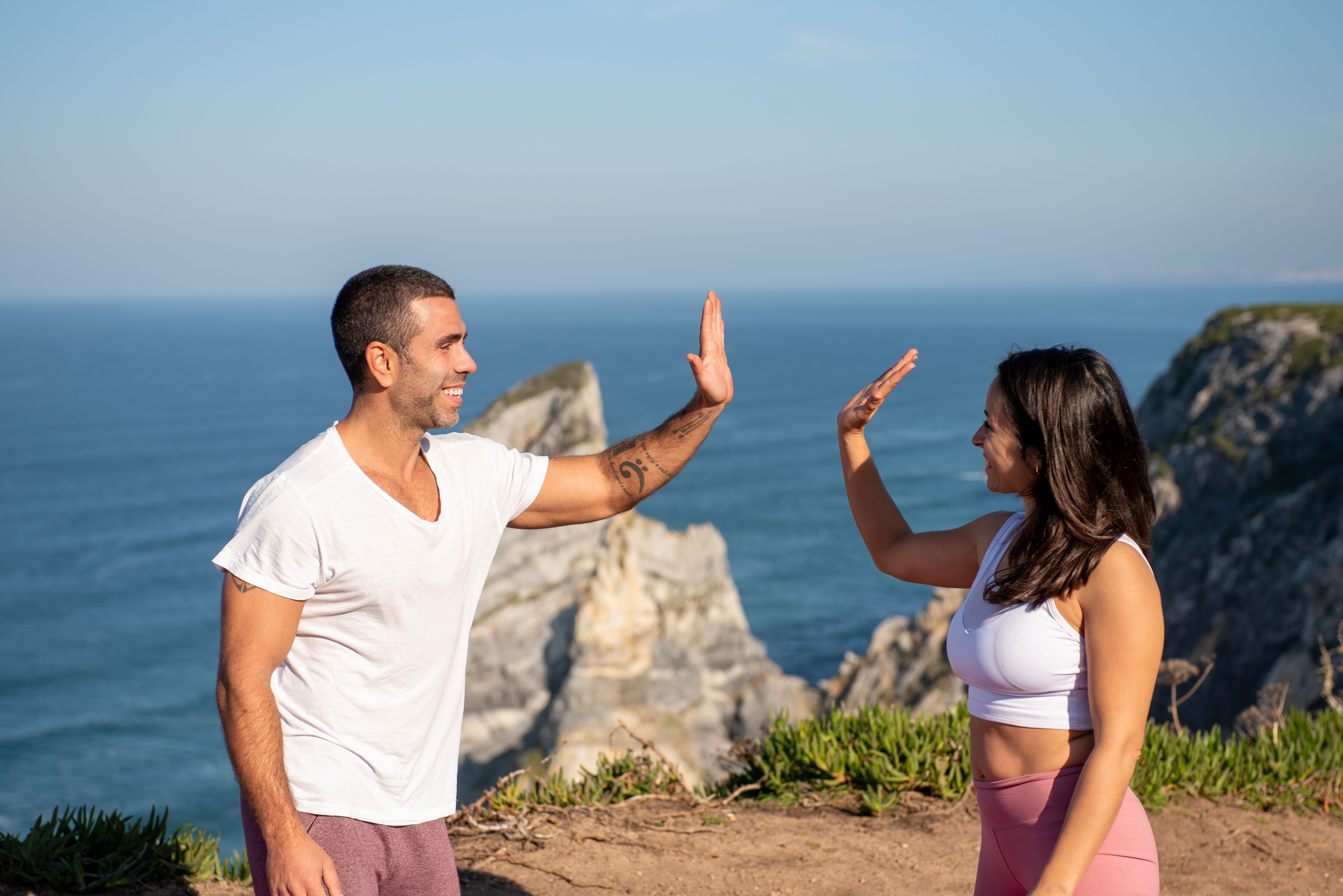 Fit couple in athletic wear high-fiving by the sea on a sunny day in Portugal.