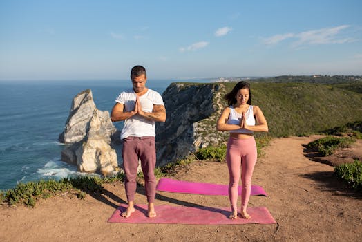 Two adults practicing outdoor yoga meditation near a stunning sea cliff in Portugal.