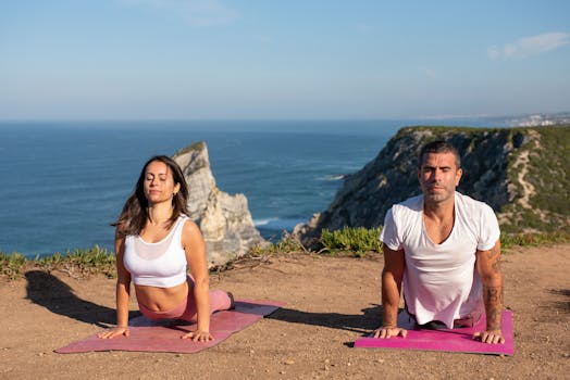 A man and woman performing yoga on scenic coastal cliffs in Portugal.