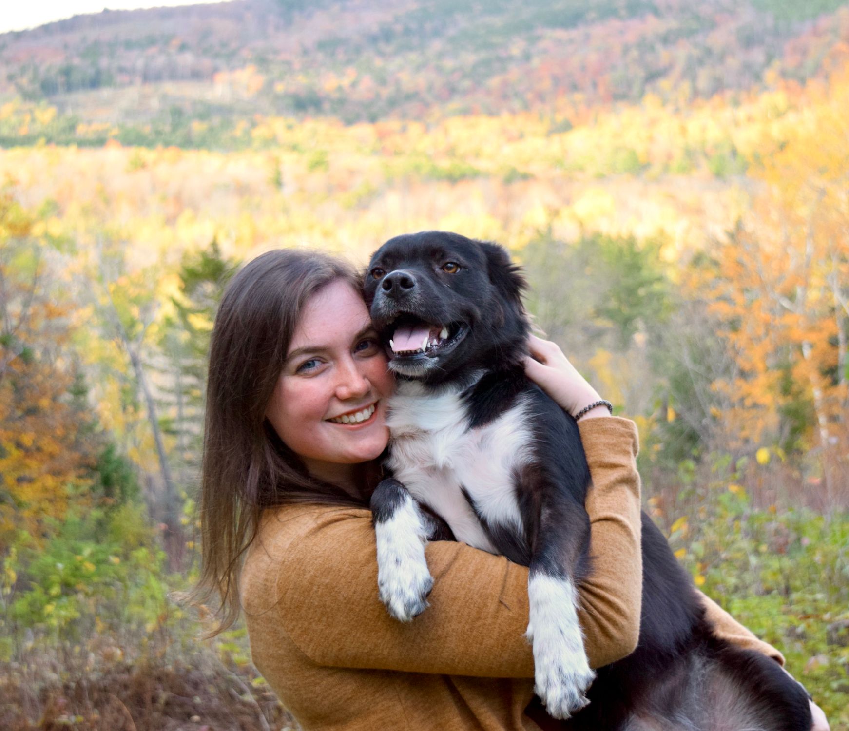 Happy woman holding her dog outdoors during fall with scenic background.
