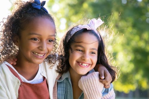 Free Two cheerful girls with arms around each other enjoying a sunny day outdoors, embodying friendship and happiness. Stock Photo