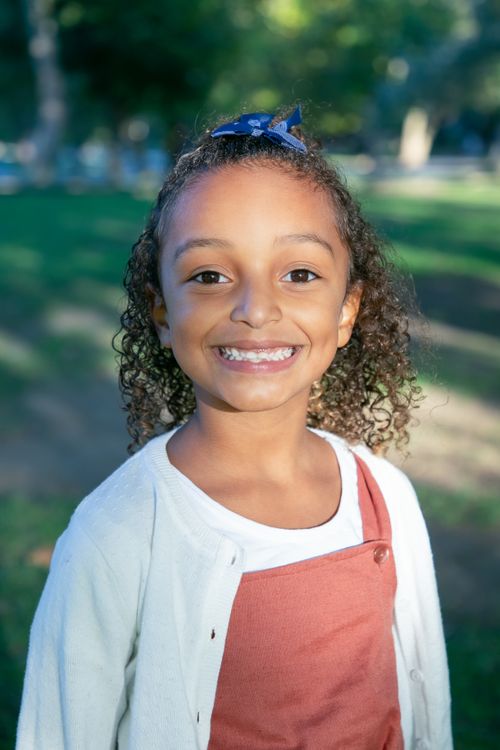 Free A cheerful girl with curly hair smiling at the camera during a sunny day in the park. Stock Photo