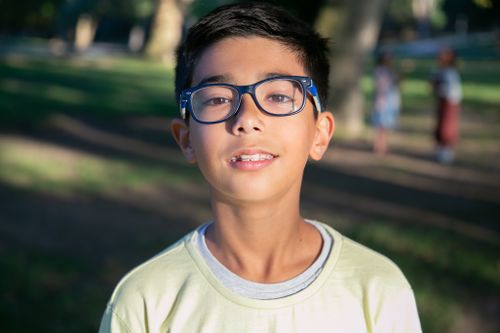 Free Close-up portrait of a young boy wearing glasses in a sunny park, capturing a natural moment Stock Photo