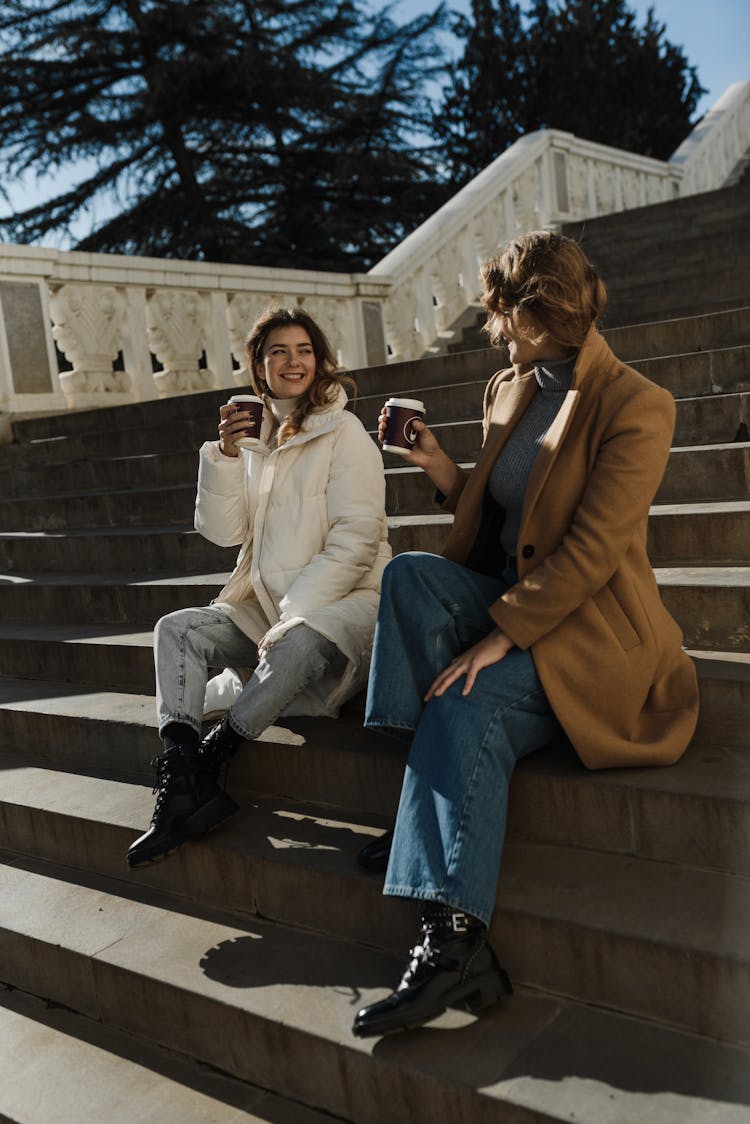 Women Sitting On Stairs While Holding Disposable Cups