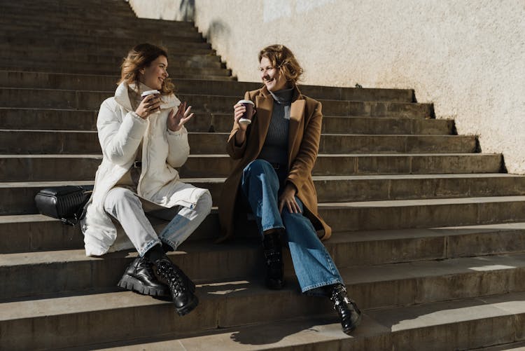 Women Holding Disposable Cups While Sitting On Stairs