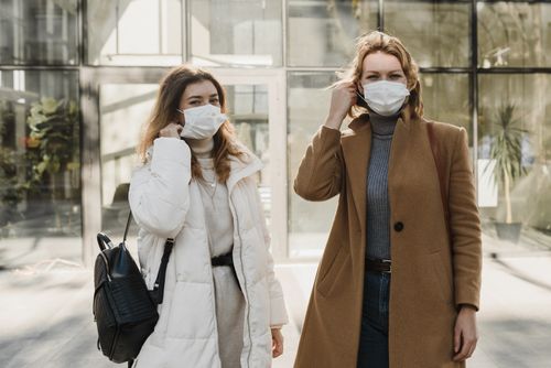 Free Two women wearing face masks and stylish coats enjoying a sunny day outdoors. Stock Photo