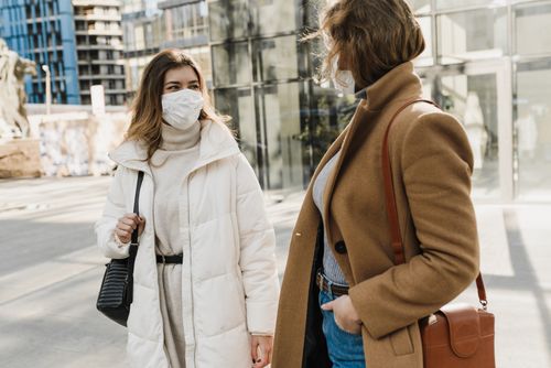 Free Two women wearing coats and face masks walking outdoors, embodying pandemic life. Stock Photo